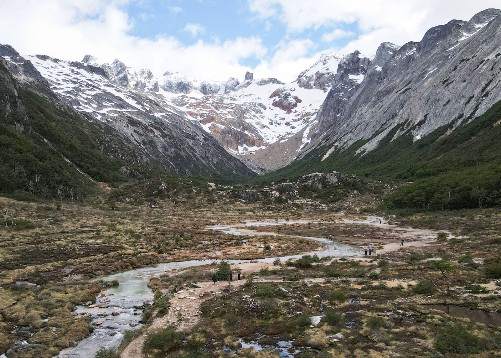 Sendero a Laguna Esmeralda atravesando los turbales del valle junto a un arroyo, con montañas nevadas de la Cordillera de los Andes de fondo, Ushuaia