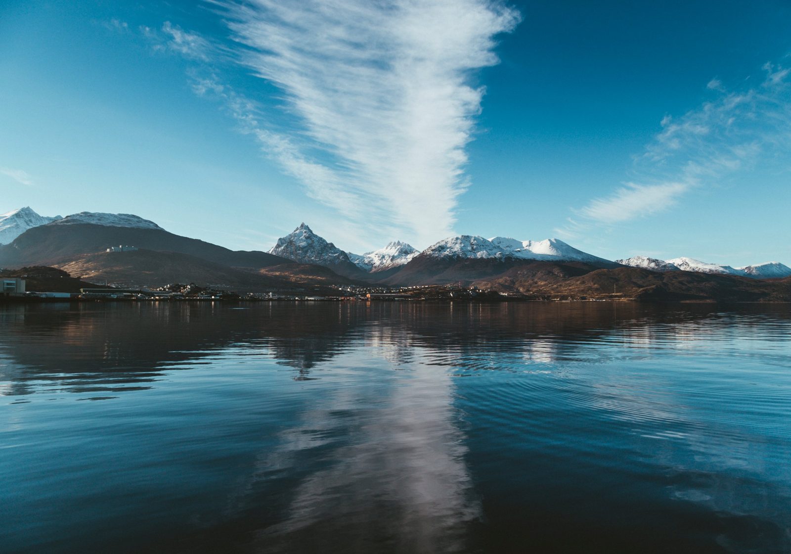 Ushuaia vista desde el Canal Beagle, con la ciudad al pie de los Andes nevados y una nube estirada sobre las cumbres